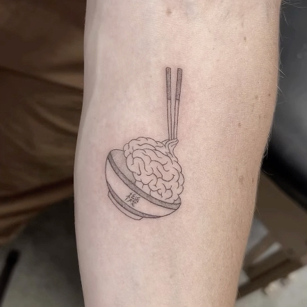 Fine-line ramen bowl tattoo holding a detailed brain with chopsticks, on the lower leg