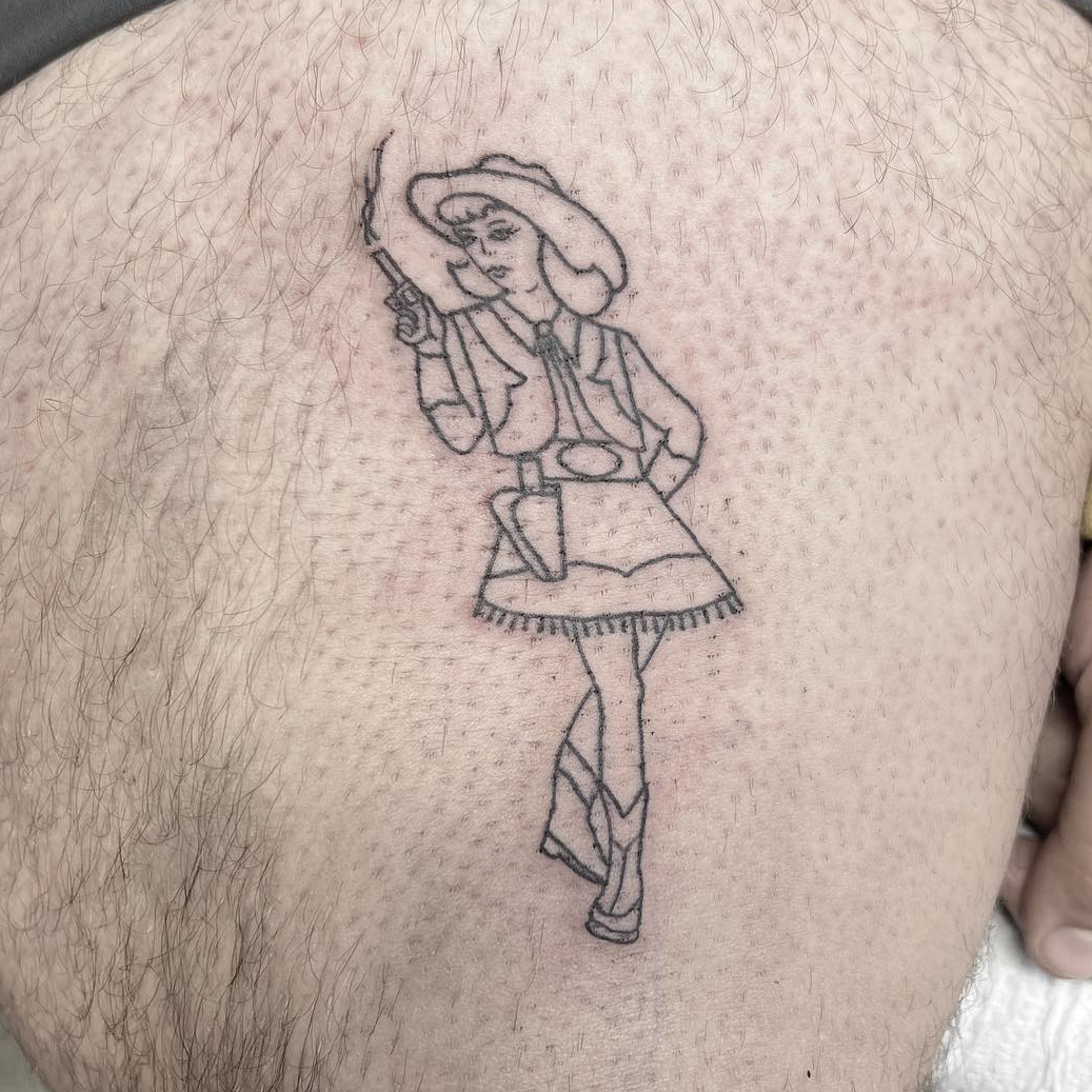 Single-needle cowgirl tattoo in a wide-brim hat firing a revolver, on the thigh