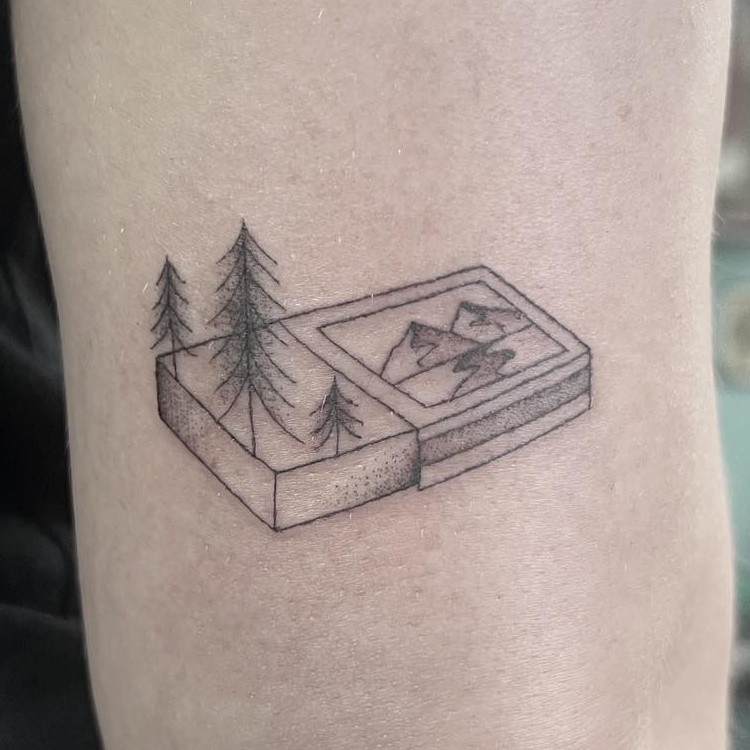 Fine-line isometric block diorama tattoo with pine trees and a mountain scene, on the upper arm