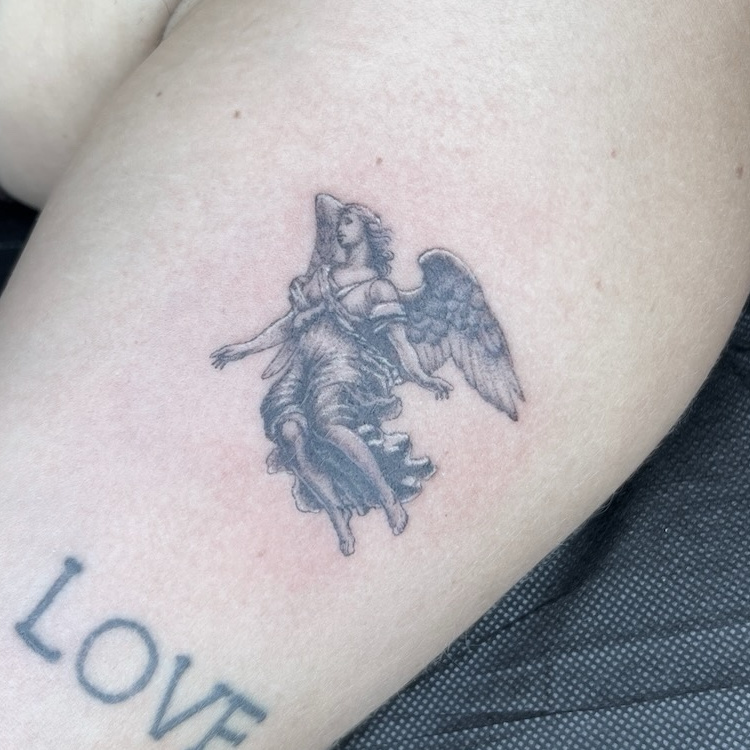 Fine-line black-and-gray winged angel tattoo with flowing robes on upper thigh