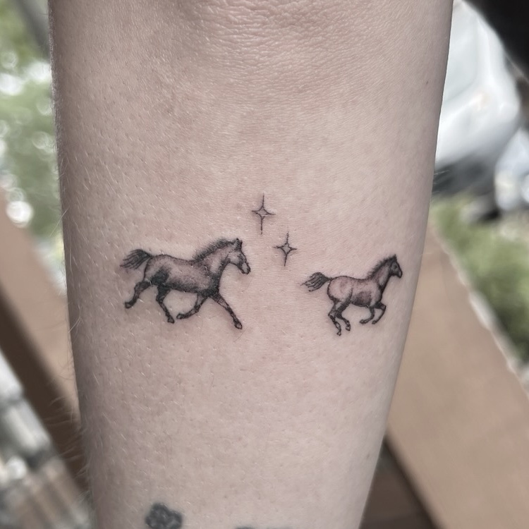 Fine-line galloping horses tattoo with stars on forearm in black and gray