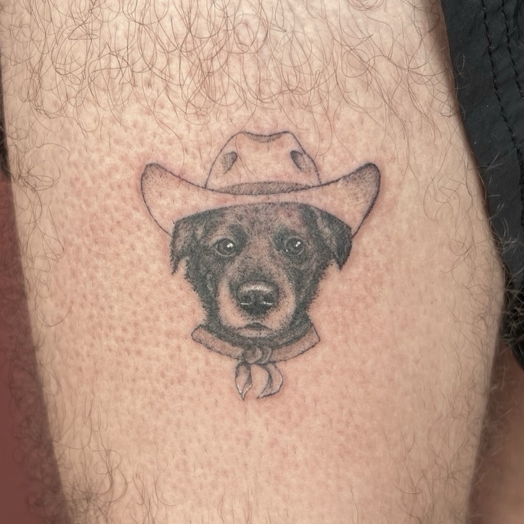 Fine-line dog wearing cowboy hat tattoo on thigh